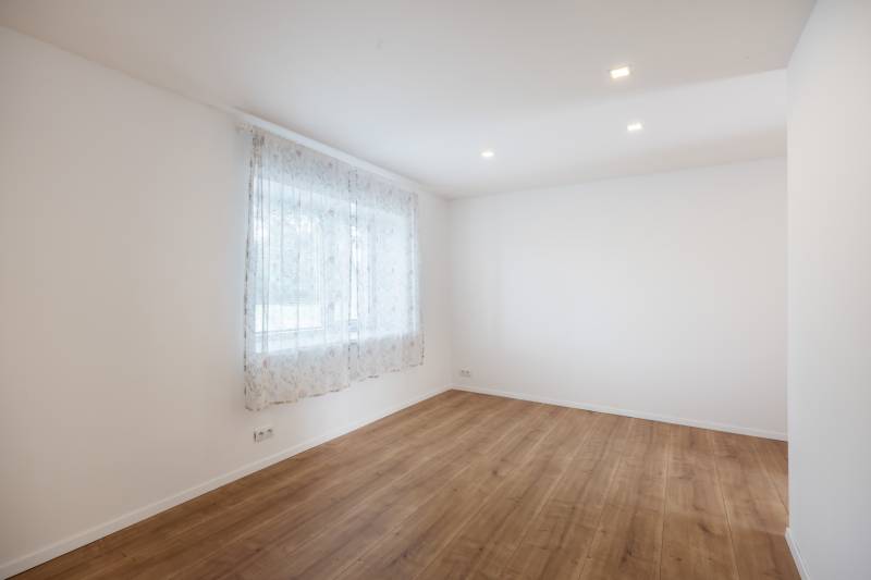The interior of an empty room in a family house with wooden flooring and a curtain on the window.