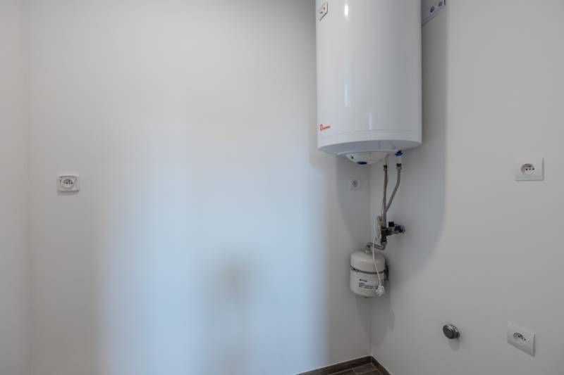 A boiler in the bathroom of a family house with white walls and tiles.
