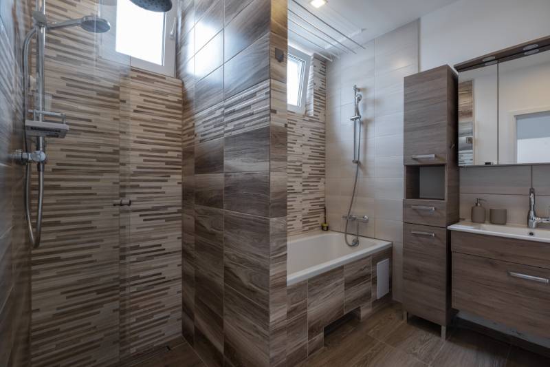 Bathroom with a bathtub, shower, and cabinets in a family house.