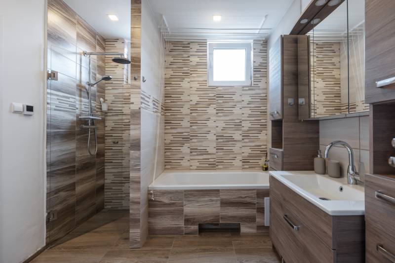 A bathroom in a family house with a bathtub, shower, and wooden cabinets.