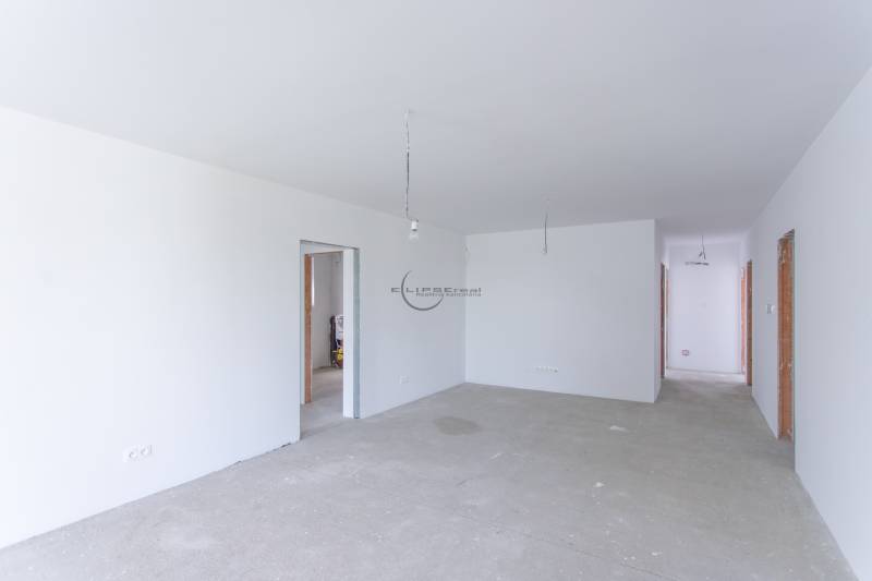 Spacious room in a family house with white walls and raw flooring.