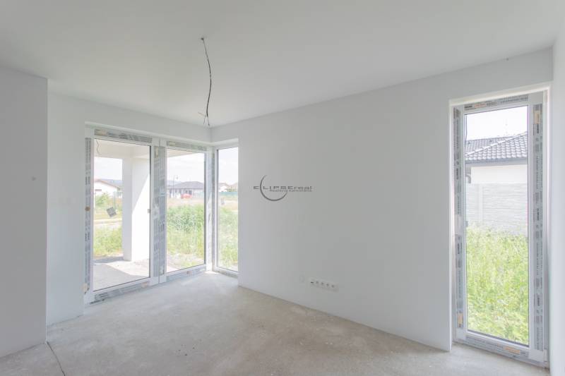 A spacious room with large windows and a raw floor in a family house.