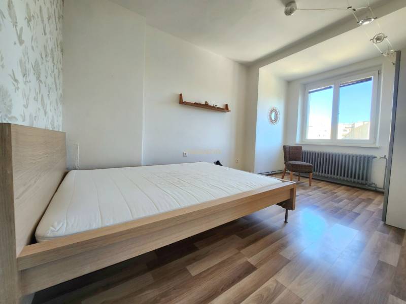 Bedroom in a 2-room apartment with wooden flooring, a bed, and a chair.
