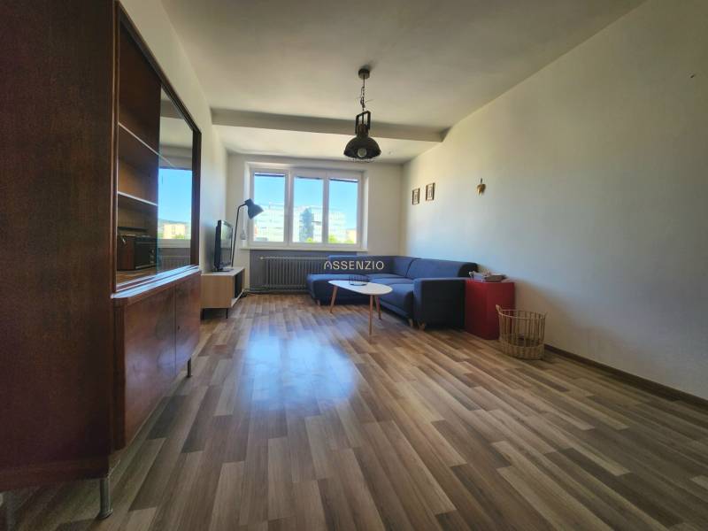 Living room in a two-room apartment with a corner sofa and wooden flooring.