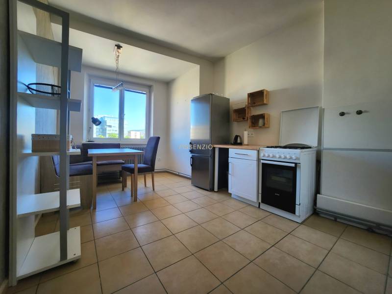 A kitchen in a 2-room apartment with a dining table, appliances, and a large window.