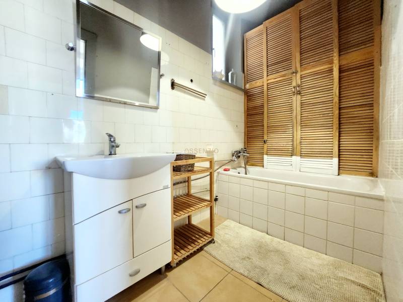 A bathroom in a 2-room apartment with a bathtub, a sink, and a wooden cabinet.