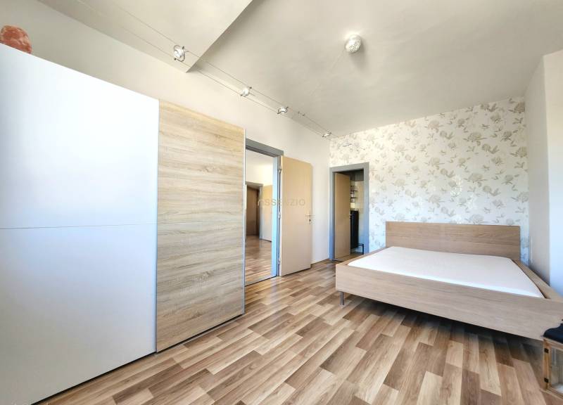 Bedroom with wooden flooring, a bed, and a built-in wardrobe in a two-room apartment.