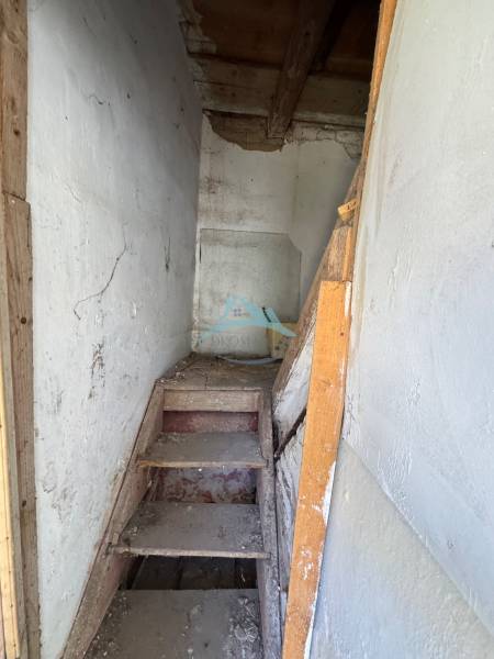 Narrow wooden staircase in commercial premises with white walls and beamed ceiling.