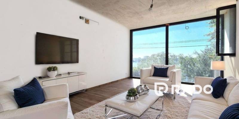 Living room in a cottage with large windows, white furniture, and a TV on the wall.