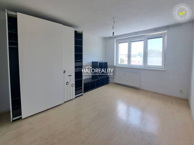 Spacious studio apartment with wooden flooring and large windows, equipped with storage spaces.