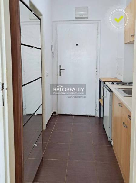 A kitchen in a studio apartment with white walls, tiles, and wooden furniture.