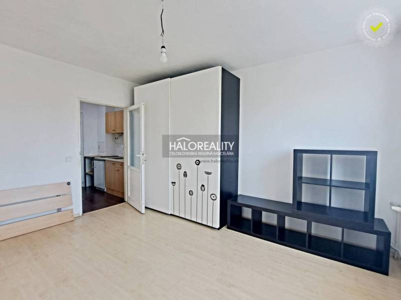 Studio apartment with white furniture, opening into a small kitchen; empty space, bright walls.