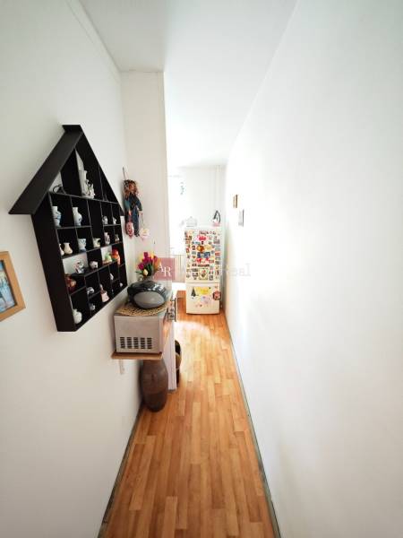A narrow hallway with a wooden floor, shelves, and a small refrigerator in a two-room apartment.