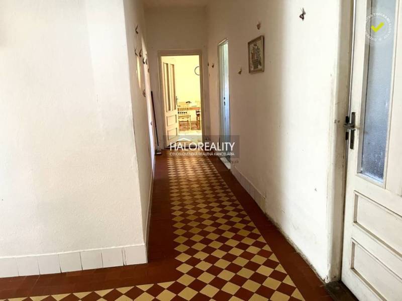 A hallway in a family house with tiles leading to a room with furniture.