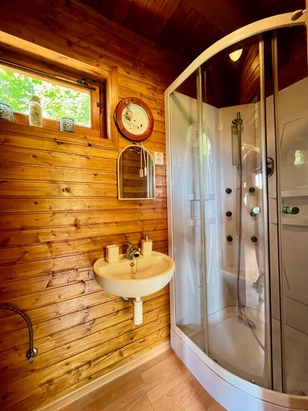 A bathroom in a family house with wooden paneling, a shower corner, and a window.