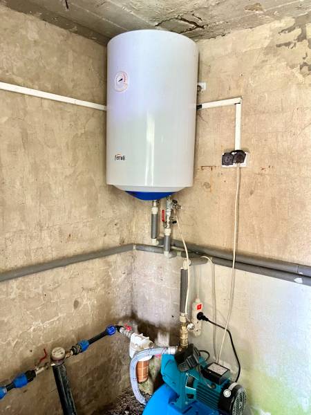 Boiler on the wall and pump in the corner in a family house.