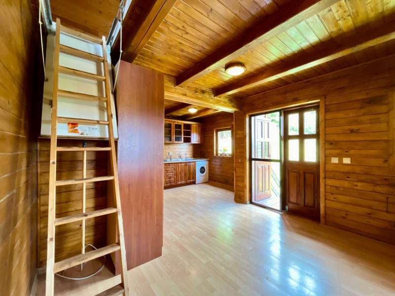 Interior of a family house with wooden walls, flooring, kitchen unit, and stairs to the upper floor.
