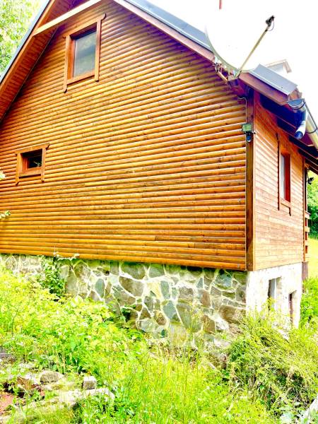 A wooden family house in Štefultov with a stone foundation surrounded by greenery.