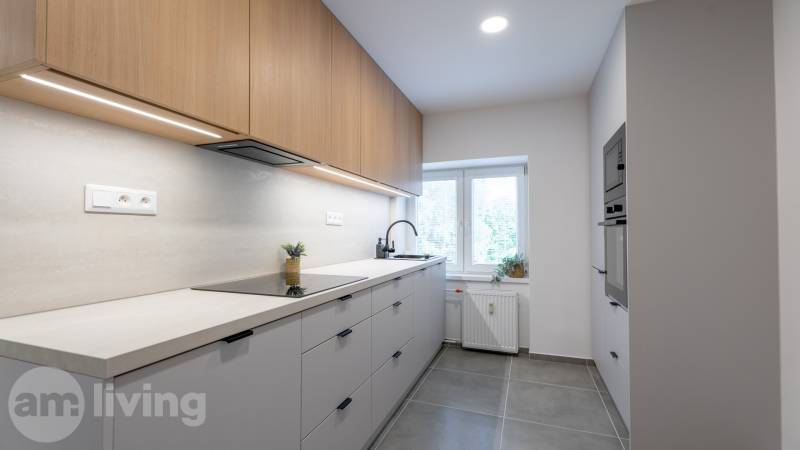 A kitchen in a studio apartment with modern equipment, light cabinets, and a large window.
