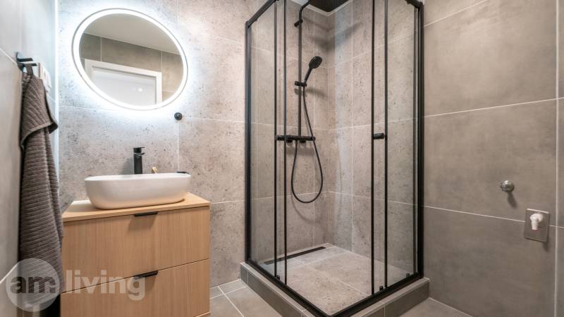 Bathroom with a square shower enclosure, light-colored sink, and ambient lighting in a studio apartment.