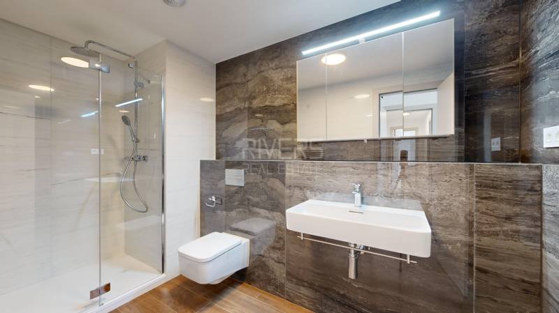 A bathroom with a shower, sink, and mirror in a 4-room apartment.