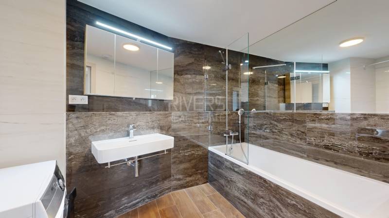 A bathroom in a 4-room apartment with a bathtub, sink, and washing machine, wooden and stone tiles.