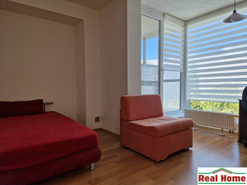 A room in a family house with a red sofa and an armchair, large window with horizontal blinds.