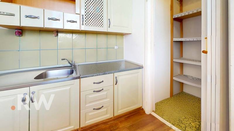 A kitchen in a studio apartment with white cabinets, a sink, and a built-in pantry.