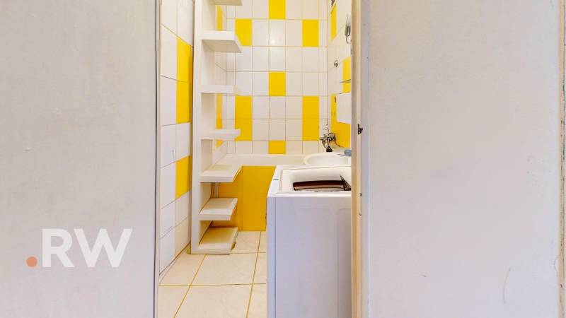 A bathroom with a washing machine and shelves in yellow and white tones in a studio apartment.