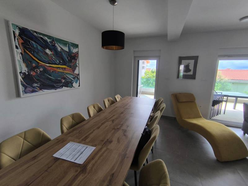 Dining room in a 4-room apartment with a long table, paintings, and a comfortable armchair.