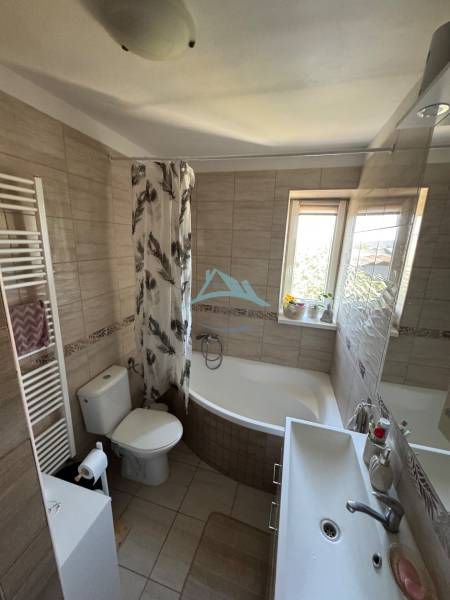 A bathroom in a 3-room apartment with a bathtub, a sink, and a window for natural light.