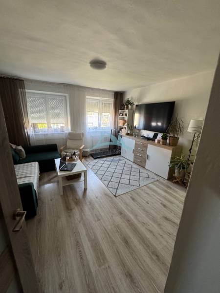 Living room in a 3-room apartment with a sofa, television, table, and wooden floor.