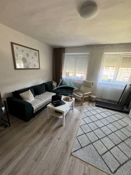 A bright living room in a three-room apartment with a sofa, an armchair, and a table on a light floor.