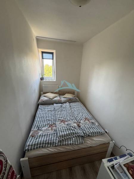 A small bedroom with a narrow window and a bed in a three-room apartment.