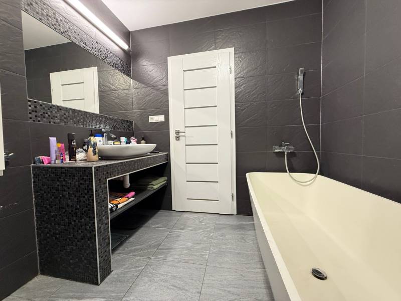 A bathroom in a 4-room apartment with dark tiles, a sink, and a bathtub.