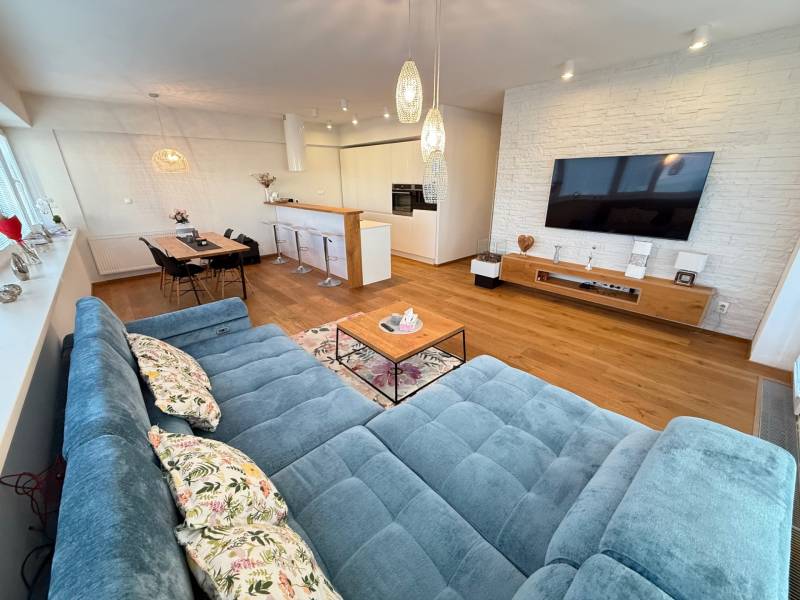 A spacious living room of a 4-room apartment with a comfortable couch and a TV on the wall.