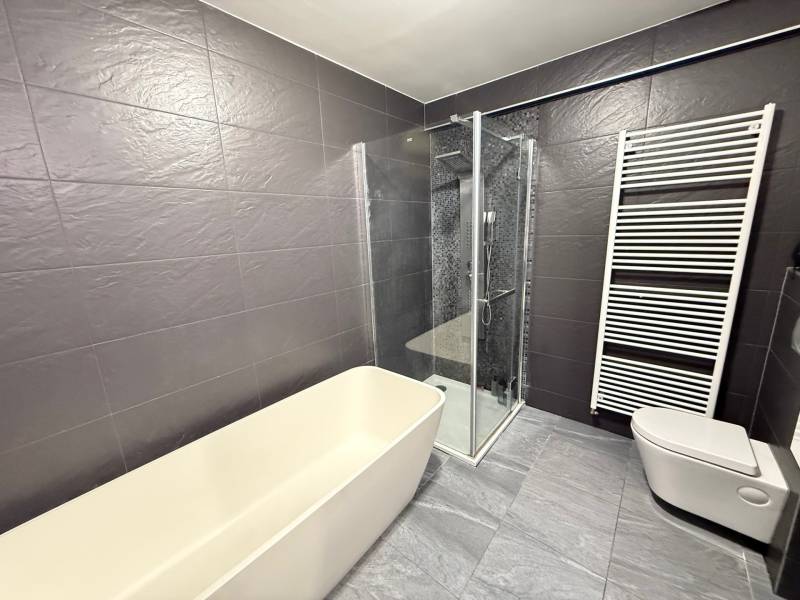 A bathroom in a 4-room apartment with a bathtub, shower, and wall heating.