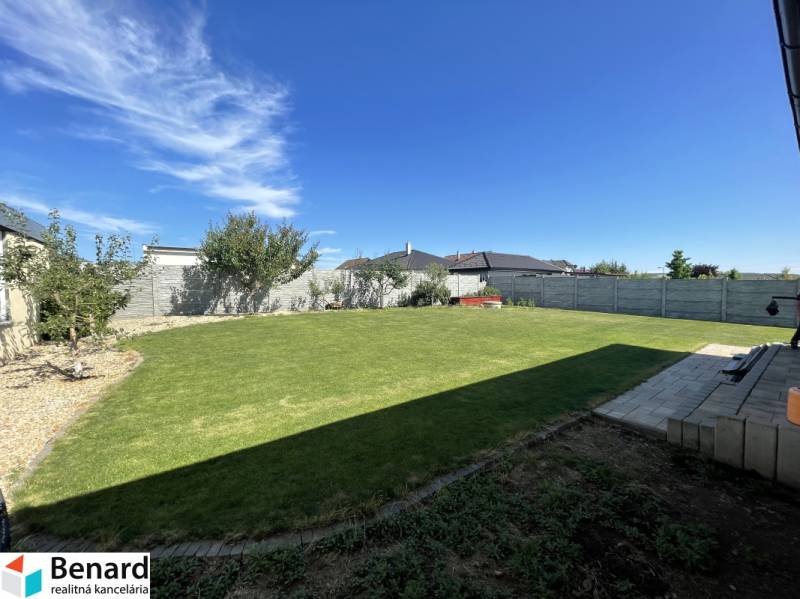 A garden of a family house in Prešov with a lawn, trees, and a terrace under a blue sky.