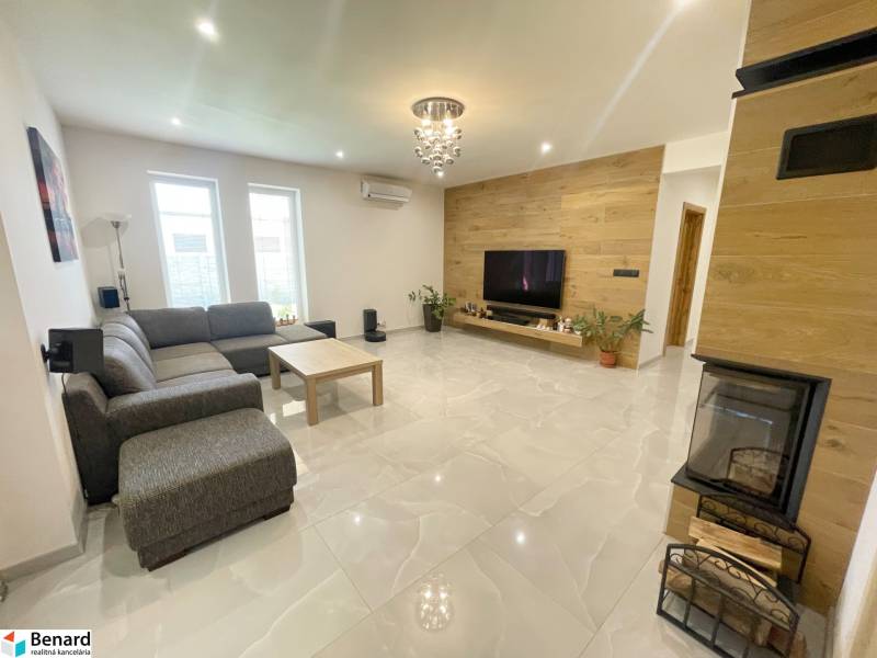 Living room in a family house with a fireplace, corner sofa, and television on a wooden wall.