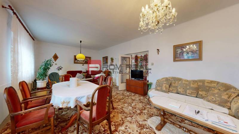 Living room in a family house with furniture, carpet, chandelier, curtains, and paintings.
