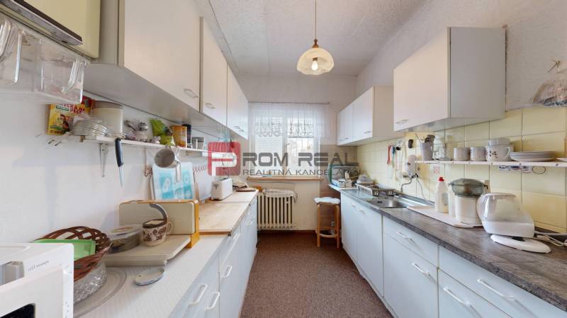 A kitchen in a family house with white cabinets, appliances, and a window with a white curtain.