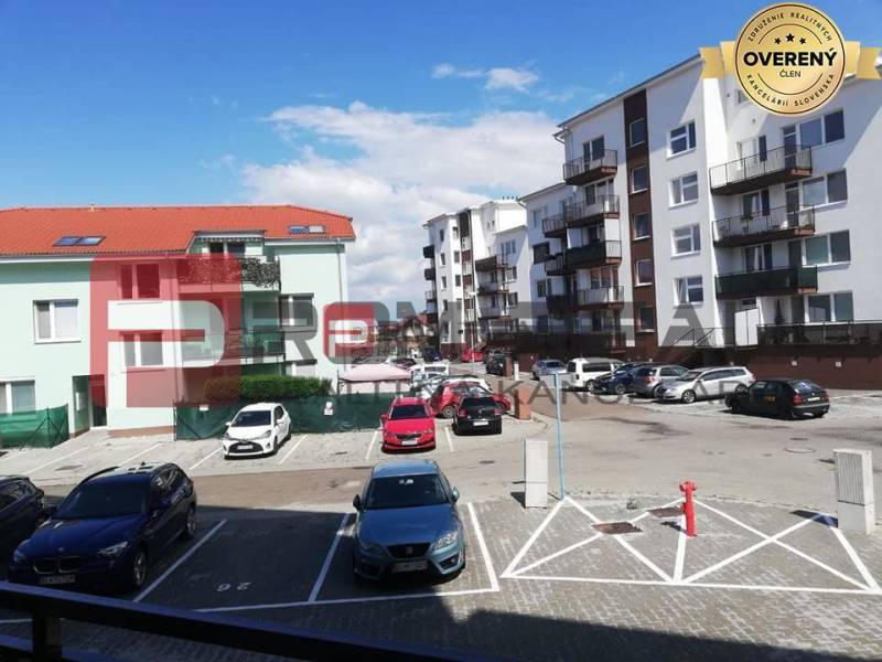 Parking lot on Slavomírova Street with cars in front of buildings in an urban environment.