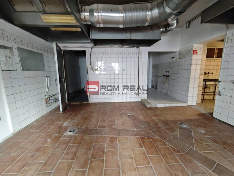 Commercial premises with tiles and cladding, containing ventilation ductwork and a door to the back area.
