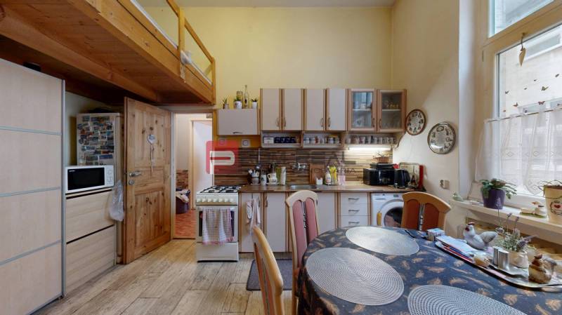 A kitchen in a 2-room apartment with a wooden gallery, dining table, and cabinets.