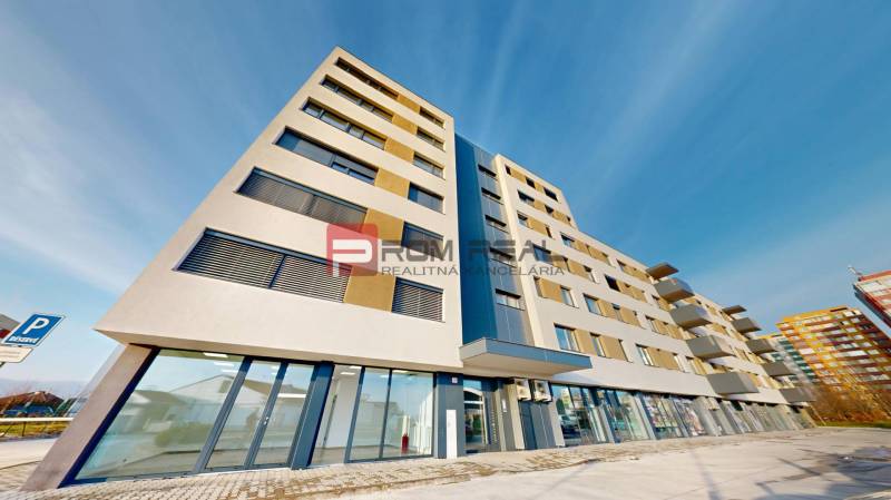 A building with commercial spaces on Obchodná Street in Pezinok, under a blue sky.