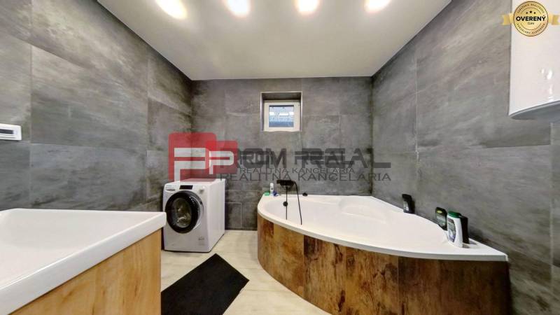 A bathroom with a bathtub and a washing machine in a family house. Gray walls with light floors.