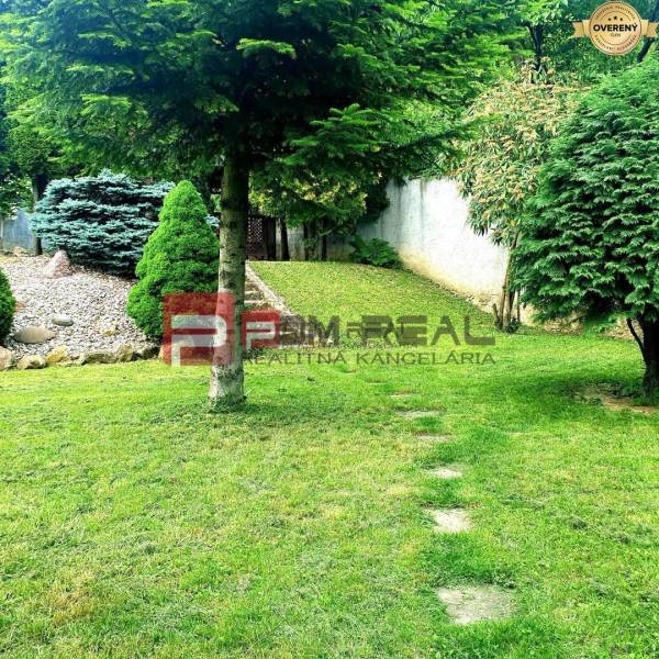 The garden of a family house in Píla with trees, grass, and a rockery.