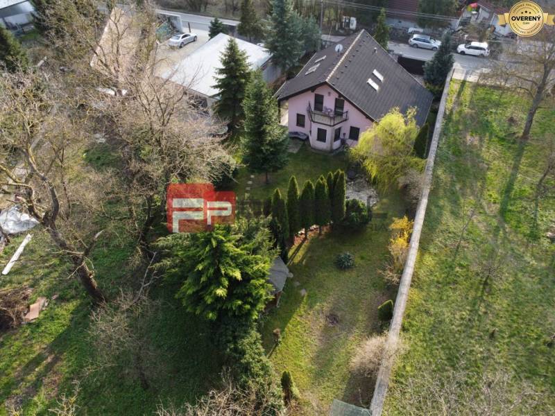 A family house in Píla surrounded by trees with a landscaped garden and neighboring buildings.