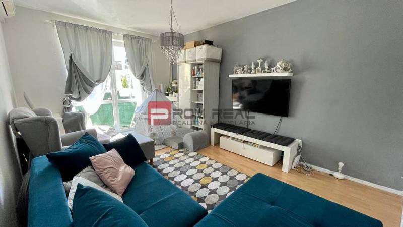 Living room in a three-room apartment with a blue sofa and a TV on the wall.