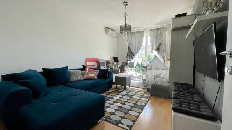 Living room of a three-room apartment with a sofa, carpets, and a window with long curtains.